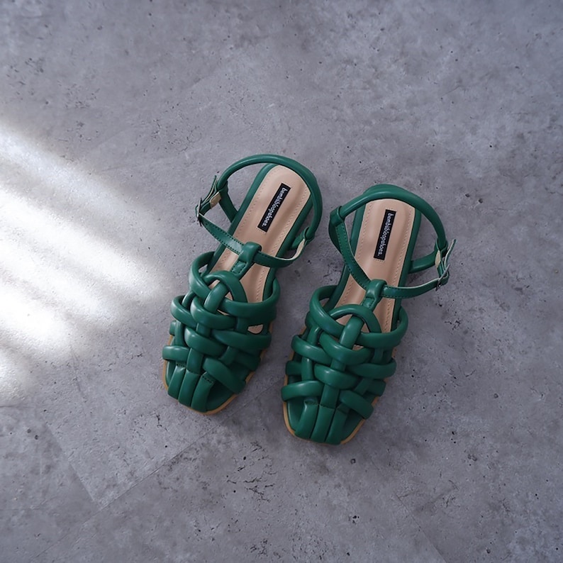 May include: A pair of green woven sandals with ankle straps. The sandals have a woven design and a flat sole.