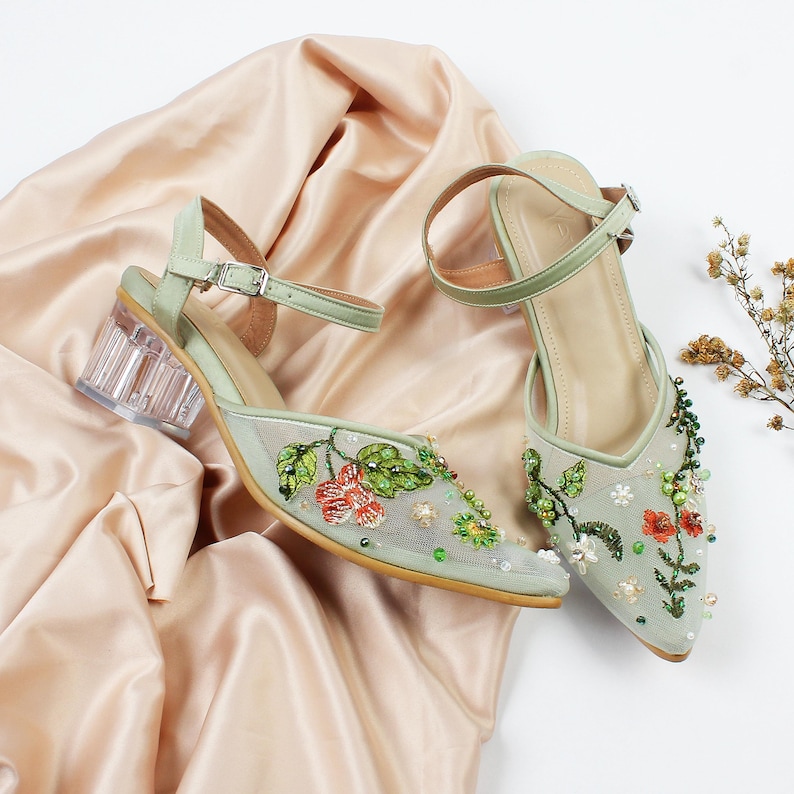 K&ouml;nnte beinhalten: Ein Paar hellgr&uuml;ne Schuhe mit Absatz, floraler Stickerei und Perlenbesatz. Die Schuhe haben transparente Abs&auml;tze und Kn&ouml;chelriemen.