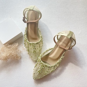 May include: A pair of light green, pointed-toe heels with ankle straps. The shoes are adorned with delicate lace and small, light green beads. The heels have a medium height and a buckle closure. The overall design is elegant and suitable for special occasions.