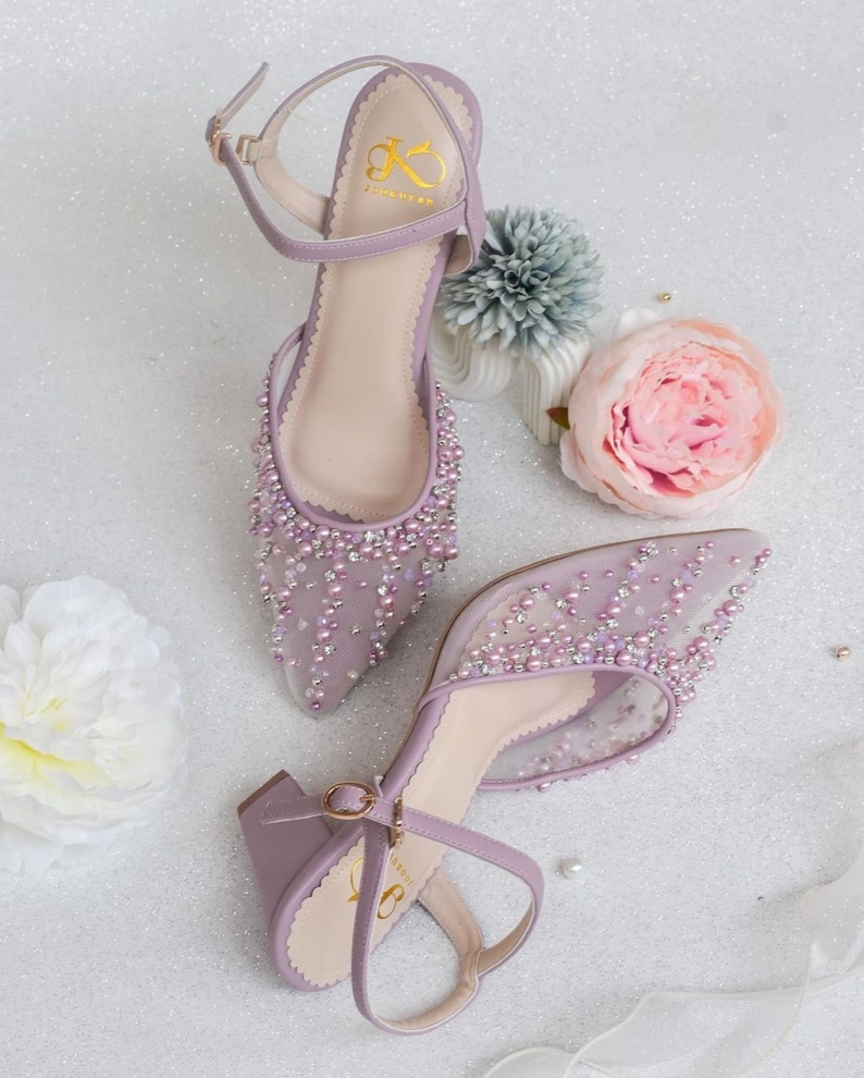 May include: A pair of lavender high-heeled shoes with a delicate mesh fabric and pearl embellishments. The shoes have a pointed toe and an ankle strap with a gold buckle.