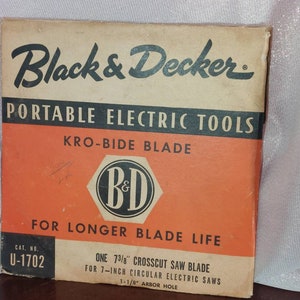 May include: A vintage box for a Black & Decker Kro-Bide saw blade. The box is orange and brown with black text. The text reads "Black & Decker Portable Electric Tools Kro-Bide Blade For Longer Blade Life Cat. No. U-1702 One 7 3/8" Crosscut Saw Blade For 7-inch Circular Electric Saws 1-1/8" Arbor Hole".