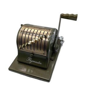 May include: An olive green vintage Paymaster cash register. The register has a crank handle, keys, and a display with dollar and cent indicators. The word "Paymaster" is printed on the front.