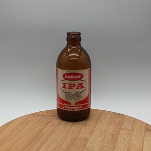 May include: A brown glass bottle with a red and white label that reads "Labatt IPA". The bottle has a rounded shape and a narrow neck. The label also includes the text "...the original".