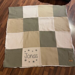 Könnte beinhalten: Eine beige und grüne Waffel-Babydecke mit einem weißen Quadrat in der Mitte, auf dem "Jonas" in grauer Stickerei mit Sternen steht.
