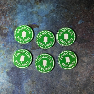 Könnte beinhalten: Sechs grüne und weiße runde Aufkleber mit dem Text "Ziel gesichert" und einem kleinen weißen Symbol eines Gebäudes.