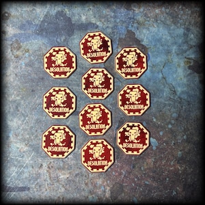 May include: A collection of eleven octagonal tokens with a red and cream color scheme. Each token features a skull graphic and the word "DESOLATION". The tokens are arranged on a textured blue surface.