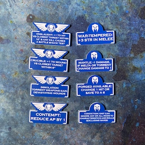 May include: A collection of blue and white game tokens with various text descriptions. The tokens feature a winged skull emblem and phrases like "ONSLAUGHT" and "WAR-TEMPERED". These tokens are likely used in a tabletop strategy game.