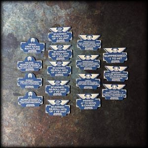 Può includere: Una collezione di gettoni di gioco blu e bianchi con varie descrizioni testuali. I gettoni hanno una forma rettangolare con la parte superiore curva e un emblema bianco. Il testo include frasi come "Scanned: Re-roll Hits of 1 vs Unit" e "Bastion".