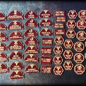 May include: A collection of laser-cut wooden game tokens with burgundy and tan colors. The tokens feature various text descriptions and symbols, including "Scorched," "Molten Metal," and "Daemonic Point." The tokens are designed for tabletop gaming.