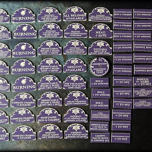 Puede incluir: Una colecci&oacute;n de fichas de juego moradas y blancas con varias descripciones de texto. Las fichas son rectangulares y arqueadas, con fichas circulares con un s&iacute;mbolo de ojo. El texto incluye frases como "Burning", "+1 to Wound" y "Cannot Run".