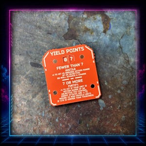 Può includere: Un gettone da gioco quadrato arancione con testo bianco che recita YIELD POINTS, FEWER THAN 7 HOSTILE, 7 OR MORE FORTIFY e varie regole di gioco. Il gettone presenta un display numerico centrale che mostra 0 e 7, con quattro fori circolari.