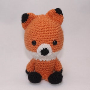 May include: A small crocheted fox plush toy with orange fur, black ears, white muzzle, and black eyes.