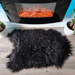 May include: A plush, long-haired black sheepskin rug with a thick, shaggy texture and an irregular, natural pelt shape. The rug features dense, wavy fibers that create a deep, dark appearance, providing a soft and voluminous surface covering.