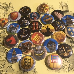 May include: A collection of 20 colourful round buttons featuring various symbols and designs from the Age of Empires II: Definitive Edition video game. The buttons are arranged in a circular pattern on a yellow background.