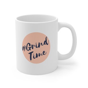 Può includere: Tazza da caffè in ceramica bianca con un cerchio color pesca e il testo "#Grind Time" in blu scuro.