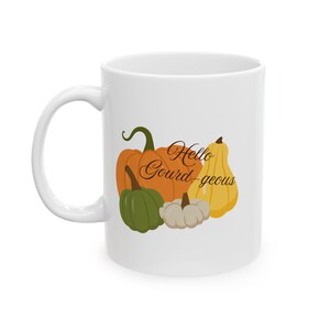 May include: White ceramic mug featuring a colorful illustration of pumpkins and gourds in shades of orange, green, yellow, and white. The mug has the text "Hello Gourd-geous" in a script font, perfect for autumn.
