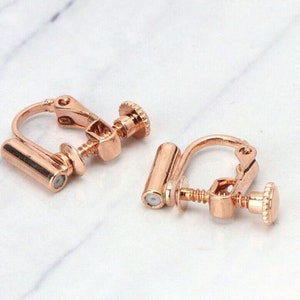 May include: A pair of rose gold clip-on earrings. The earrings have a screw-on back and a cylindrical post.