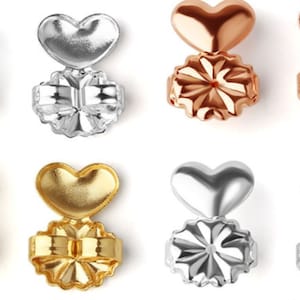May include: Six pairs of earring backs in three different colors: silver, gold, and rose gold. Each pair features a heart-shaped top and a starburst-shaped bottom.