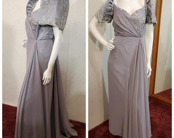 May include: A long, grey, formal gown with a sweetheart neckline and a fitted bodice. The gown has a flowing skirt and is adorned with delicate lace detailing on the sleeves and bodice.