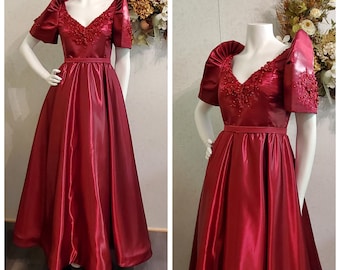 May include: A formal red satin gown with a V-neckline and short puffed sleeves. The gown has beaded embellishments on the neckline and sleeves. The gown is fitted at the waist and flows out into a full skirt.
