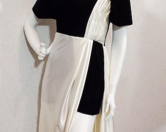 May include: A formal gown with a black velvet bodice and sleeves, paired with an ivory satin skirt. The dress features a V-neckline and a high slit, creating a striking contrast of textures and colors. The dress is displayed on a mannequin.