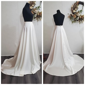 May include: A white satin skirt with a simple design. The skirt is full and flowing, with a slight train. It is perfect for a wedding or other formal event.
