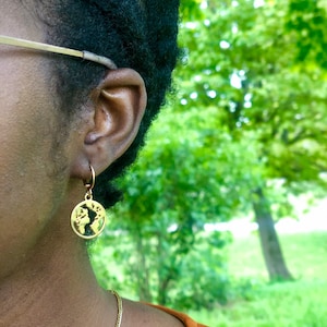 May include: A close-up of a person's ear wearing gold globe-shaped earrings. The earrings are dangling and have a delicate design.