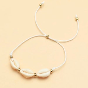 Könnte beinhalten: Weißes Armband aus Schnur mit drei weißen Muscheln und goldenen Perlen.