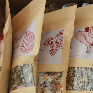 May include: Four brown paper bags with different illustrations and text. The bags contain loose leaf herbs and are labeled "Herbal Salts", "Herbs", "Yoni Steam", and "Moon Mama".