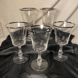 May include: Set of five clear glass wine glasses with a silver rim. The glasses have a stemmed base and a round bowl.