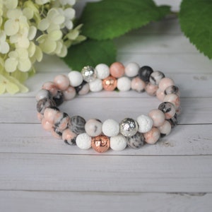 May include: A double-strand bracelet made with pink, grey, and white beads. The bracelet features a mix of smooth and textured beads, including some with a metallic finish.