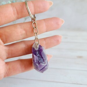 May include: Amethyst crystal keychain with a silver chain. The crystal is a deep purple color with white streaks.