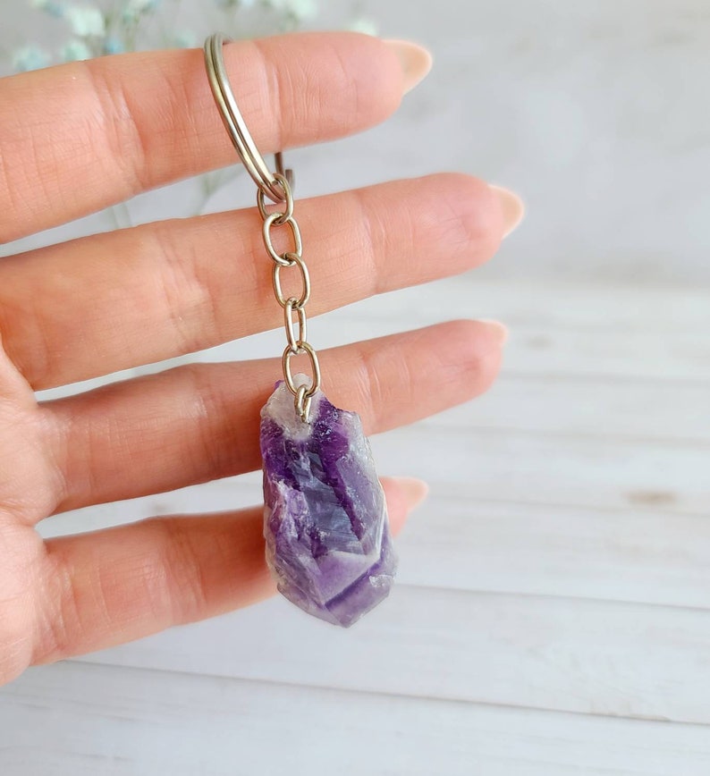 May include: Amethyst crystal keychain with a silver chain. The crystal is a deep purple color with white streaks.