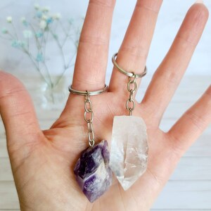 May include: Two crystal keychains, one amethyst and one clear quartz, hanging from silver key rings.