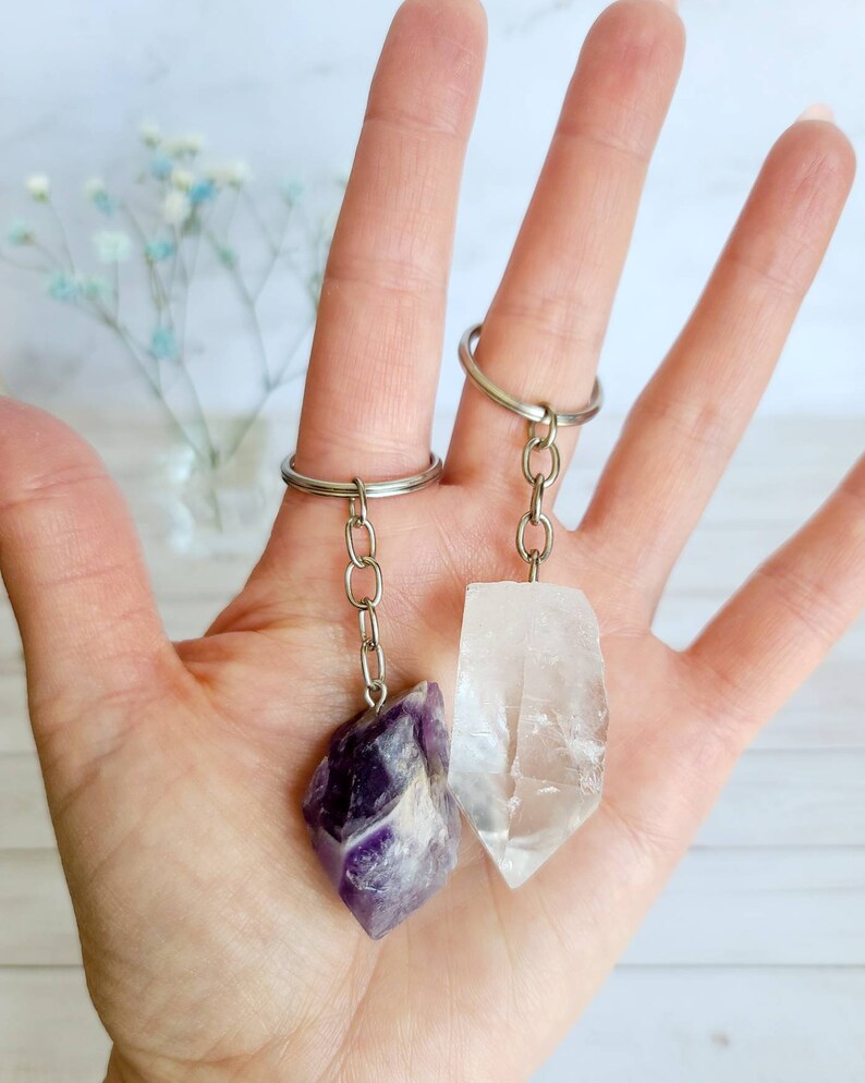 May include: Two crystal keychains, one amethyst and one clear quartz, hanging from silver key rings.