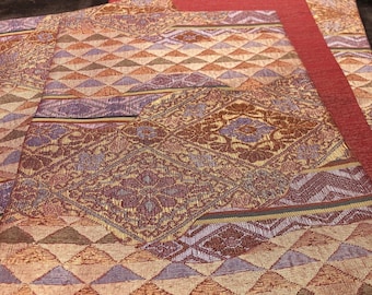 May include: A set of three placemats with a geometric pattern in shades of red, brown, gold, and purple. The placemats are made of a woven fabric with a textured surface.