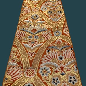 May include: A close-up of a fabric with a repeating pattern of stylized flowers and leaves in shades of orange, gold, white, blue, and black.