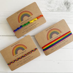 May include: Three brown cards with rainbow bracelets and the text "Pride Bracelet", "Proud to be who I am", and "It's okay to be different".