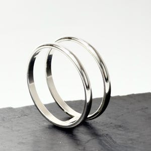 K&ouml;nnte beinhalten: Zwei polierte silberfarbene Metallringe mit einem glatten, abgerundeten Profil. Die Ringe sind aufrecht positioniert, einer leicht hinter dem anderen, und zeigen eine reflektierende, metallische Oberfl&auml;che sowie ein schlichtes, durchgehendes Ringdesign.