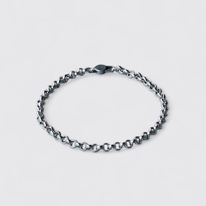 May include: A silver-toned chain bracelet featuring a series of interconnected circular links. The bracelet is arranged in a circular shape and includes a small, secure clasp mechanism at the top, showcasing a polished metallic finish throughout.