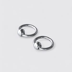May include: Two silver-toned circular rings, each featuring a smooth, polished spherical bead attached to the hoop. These metallic jewelry pieces have a reflective, high-shine finish and a simple, continuous circular design with a secure closure.