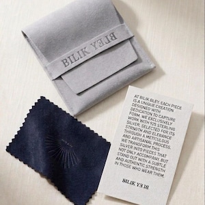 May include: A light gray velvet pouch with the text BILIK YELIB, a dark navy blue polishing cloth with a sunburst emblem, and a white rectangular card featuring printed text about 925 sterling silver and the brand name BILIK YELIB.