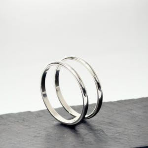 K&ouml;nnte beinhalten: Zwei polierte silberfarbene Metallringe mit einem glatten, abgerundeten Profil. Die Ringe sind aufrecht positioniert, einer leicht hinter dem anderen, und zeigen eine reflektierende, metallische Oberfl&auml;che sowie ein schlichtes, kreisf&ouml;rmiges Design.