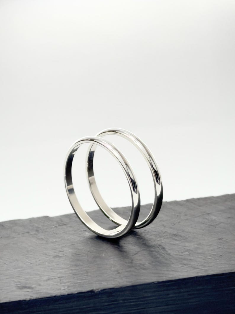 K&ouml;nnte beinhalten: Zwei polierte silberfarbene Metallringe mit einem glatten, abgerundeten Profil. Die Ringe sind aufrecht positioniert, einer leicht hinter dem anderen, und zeigen eine reflektierende, metallische Oberfl&auml;che sowie ein schlichtes, kreisf&ouml;rmiges Design.