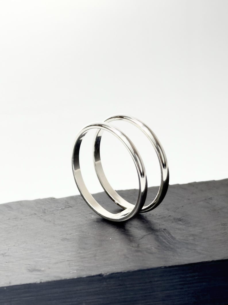 K&ouml;nnte beinhalten: Zwei polierte silberfarbene Metallringe mit einem glatten, abgerundeten Profil. Die Ringe sind aufrecht positioniert, einer leicht hinter dem anderen, und zeigen eine reflektierende, metallische Oberfl&auml;che sowie ein schlichtes, durchgehendes Ringdesign.