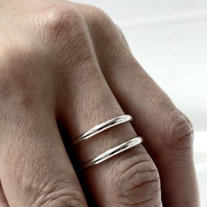 K&ouml;nnte beinhalten: Zwei polierte Silberringe an einem Finger. Jeder Ring hat ein glattes, abgerundetes Profil mit einer hochgl&auml;nzenden metallischen Oberfl&auml;che. Die Ringe sind schlicht, einfach und von gleichm&auml;&szlig;iger Dicke, was ein klares und reflektierendes Erscheinungsbild erzeugt.