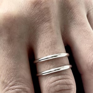 K&ouml;nnte beinhalten: Ein Set aus zwei glatten, polierten silberfarbenen Ringen, die an einem Finger getragen werden. Die Ringe haben ein schlichtes, abgerundetes Banddesign mit einer reflektierenden metallischen Oberfl&auml;che. Beide B&auml;nder sind in Form und Dicke identisch.