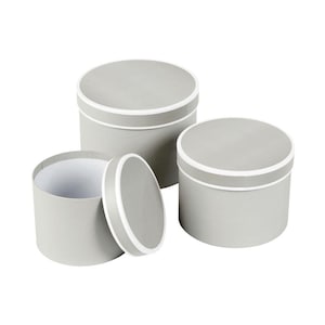 May include: Three grey, round gift boxes with white trim. One box has its lid removed, revealing a white interior. The other two boxes are closed. The boxes are different sizes and are arranged on a white background.