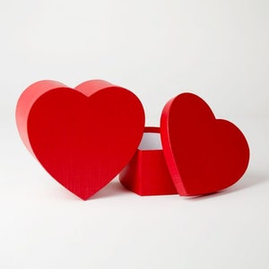 May include: A red heart-shaped box with a matching lid, open to reveal a white interior. The box is next to a larger, solid red heart. The items are on a white surface.