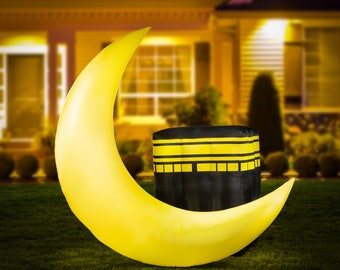 May include: A large, yellow crescent moon and a black cube with yellow stripes are set on a green lawn. The background is a blurred image of a house at night, suggesting a festive or religious theme.
